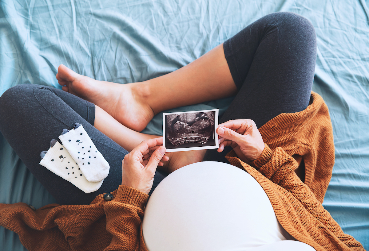Pregnant Kingwood IVF mom admiring her bump and picture from her ultrasound