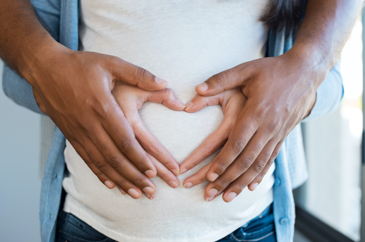 Husband and wife holding hands over pregnant belly after successful fertility treatment at our North Houston IVF clinic in the woodlands and Kingwood