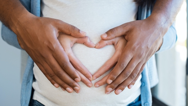 Husband and wife holding hands over pregnant belly after successful fertility treatment at our North Houston IVF clinic in the woodlands and Kingwood