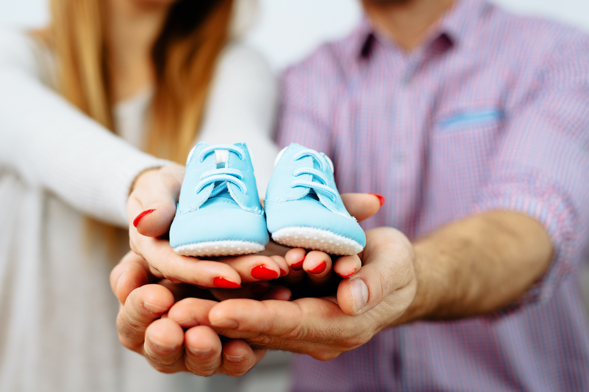 Expecting couple holding light blue baby shoes